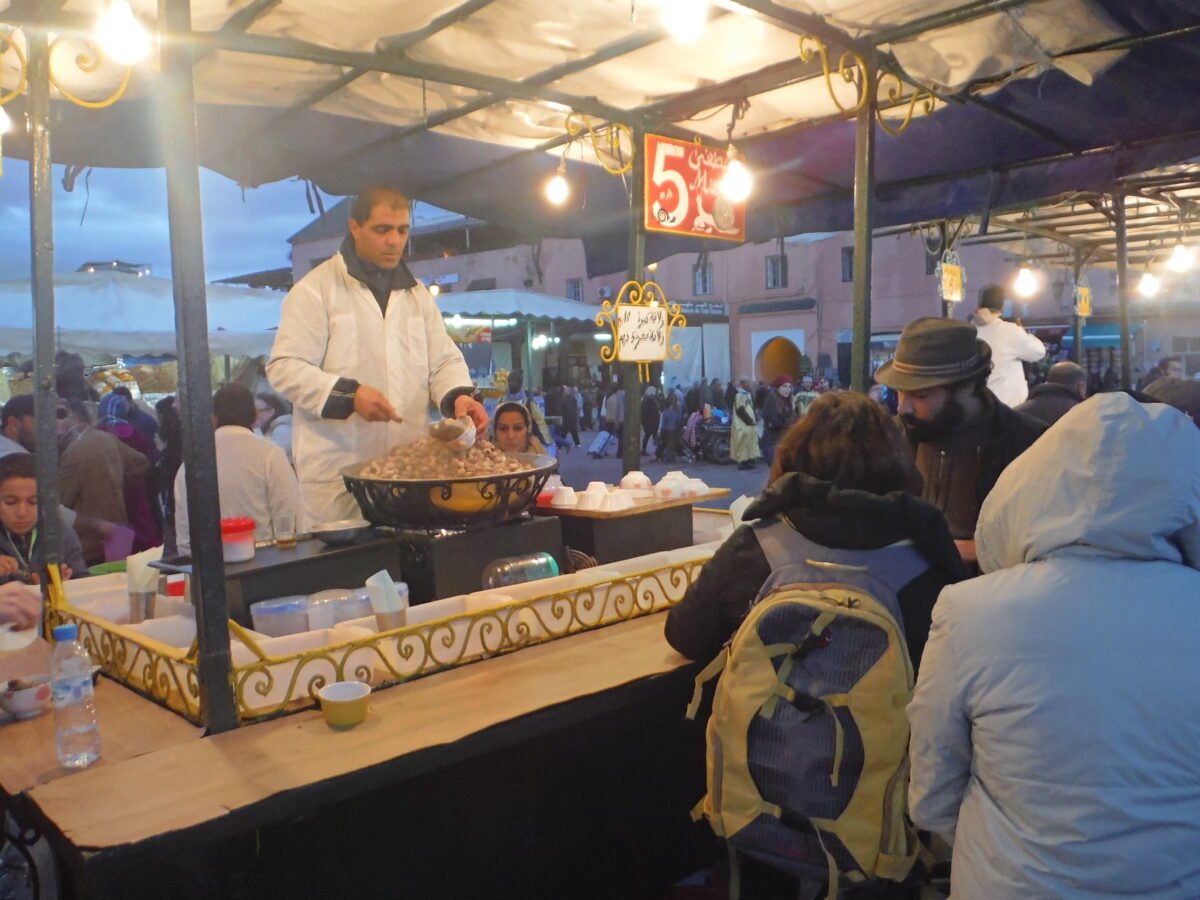 A vendor serving babbouche snail soup at a numbered stall in Jemaa el-Fna, Marrakech