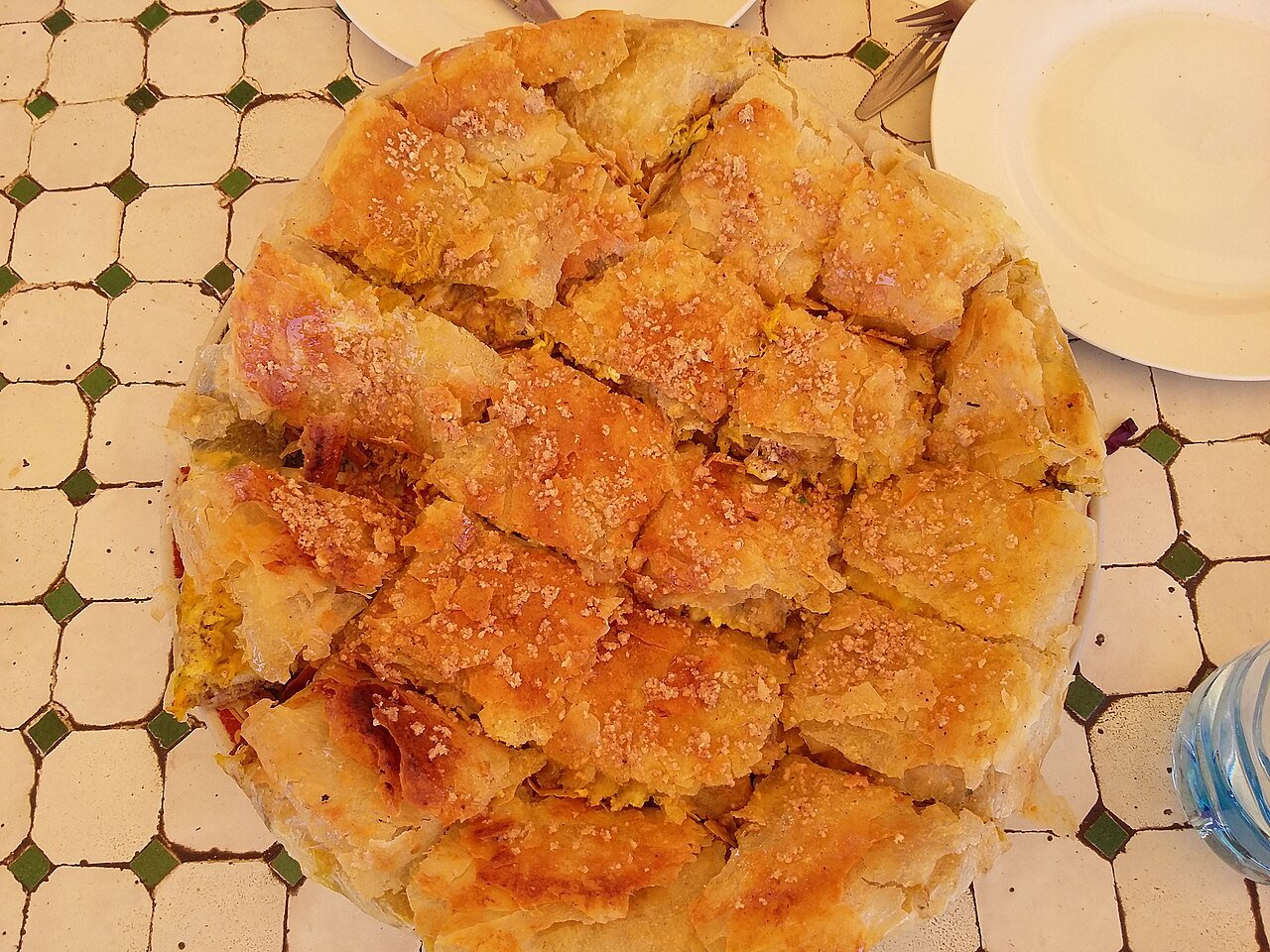 Whole round Moroccan pastilla with golden crisp warka pastry dusted with powdered sugar, served on a tiled table