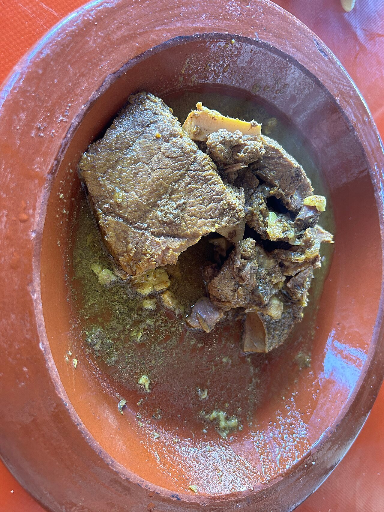 Bœuf mijoté à l'intérieur d'une urne de tanjia ouverte, la viande se détachant de l'os